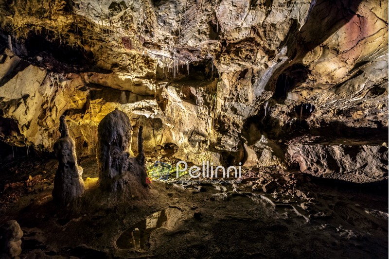cave with colourful textured walls and stalactites and stalagmite lit from behind