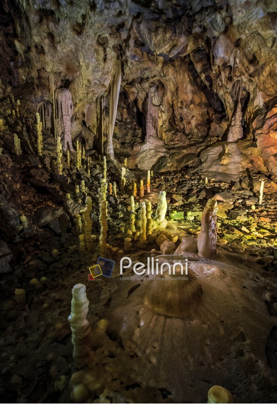 cave with colourful textured walls and stalactites and stalagmite lit from behind