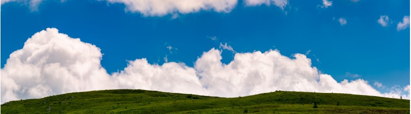cloud rising behind the grassy hills. lovely panorama of cloudscape on a blue sky