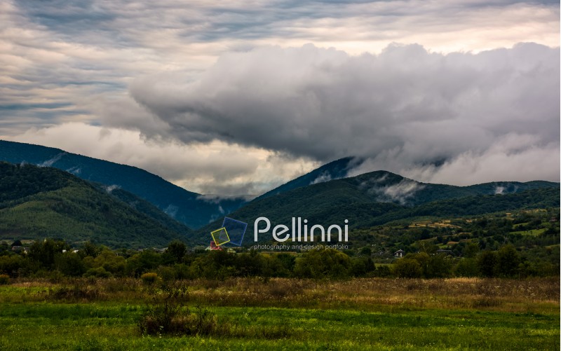 clouds rise in mountains on overcast morning. lovely countryside scenery with village at the foot on the mountain in autumn weather
