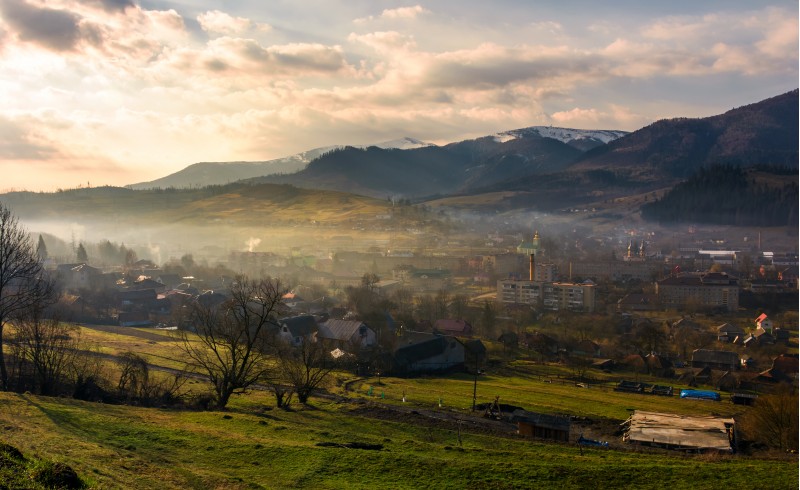cloudy and foggy sunrise in Carpathian mountains. Small town Volovets in the valley at the foot of Borzhava mountain ridge with snowy tops. lovely springtime scenery