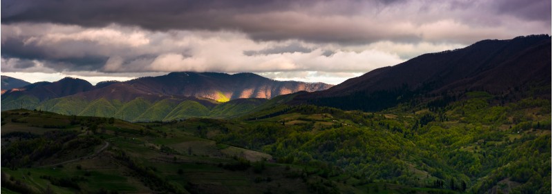 panorama of cloudy sunset in mountainous countryside. beautiful springtime landscape with ridge in the distance. rural area on grassy slopes on rolling hill in the foreground