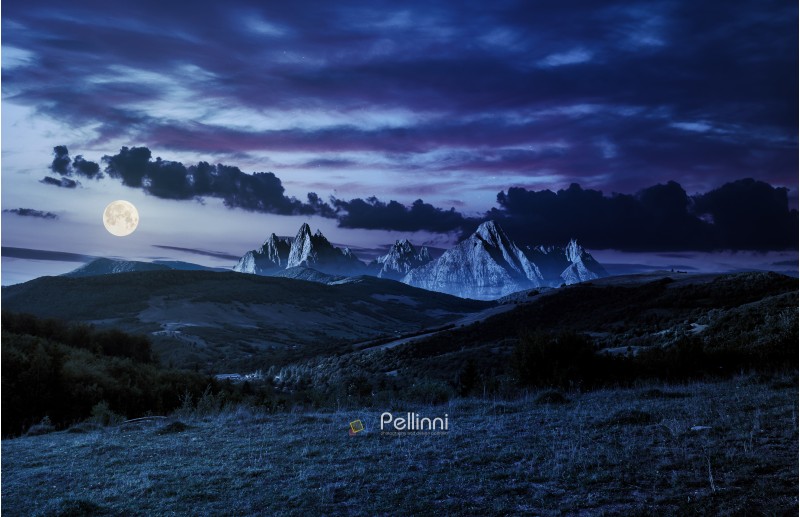 composite of countryside at night in full moon light. gorgeous cloudscape over the mountains with rocky peaks.