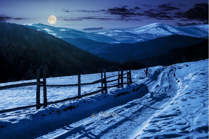 country road in to the winter mountains at night in full moon light. wooden fence along the road. composite image