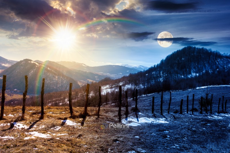 day and night time change concept. snow covered hill with barbed wire fence with sun and moon at twilight. duality and transition template