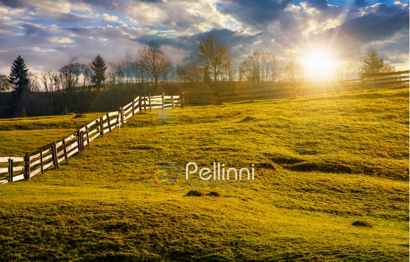 wooden fence on grassy hillside in autumn. wonderful rural scenery in fine weather with cloudy sky at sunset