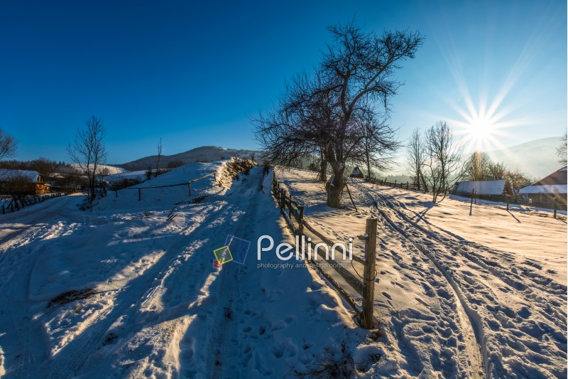 fence on the snow covered rural field on mountain slope near the village in winter day