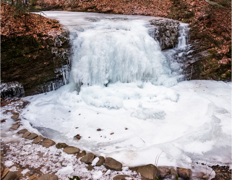 frozen waterfall on the  river among forest with brown foliage on the ground