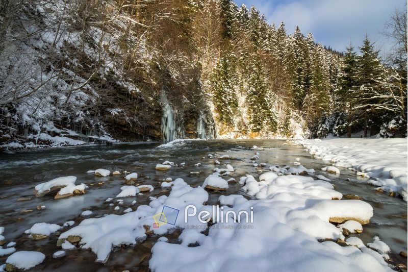frozen waterfall on the  river among forest with conifer trees and snow on the ground