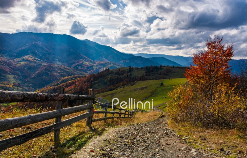 beautiful deep autumn countryside scene. wooden fence near the path through rural fields on hills in Carpathian mountainous area. Gorgeous landscape with dramatic sky over the ridge
