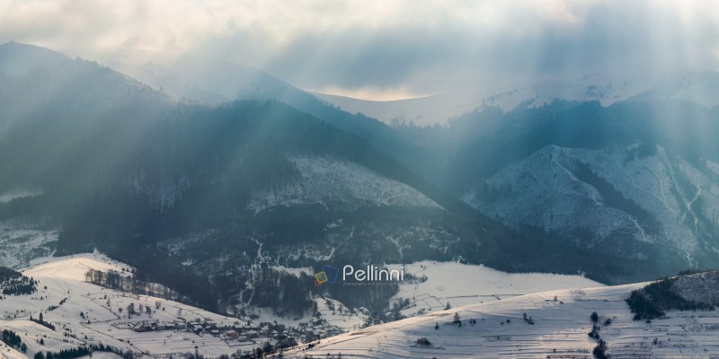 gorgeous panorama of mountains in winter. snowy hills lit with sun light through overcast sky. small village in the distant valley