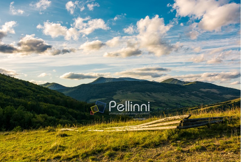 broken wooden fence on grassy hillside in mountains at sunset. landscape with beautiful cloudscape over the ridge