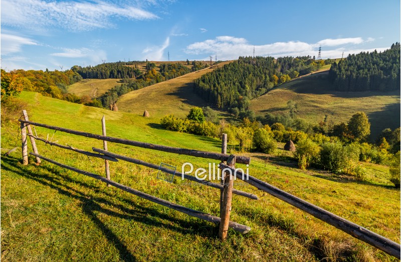 hay stacks behind the fence on rural field. lovely Carpathian hilly countryside landscape near forest in early autumn morning