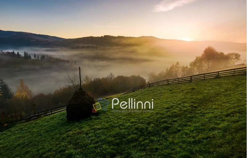 haystack and wooden fence on hillside at foggy autumn morning in mountains. beautiful rural scenery