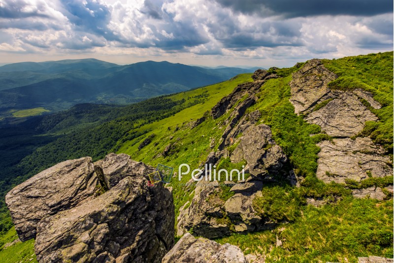landscape with grassy meadow with giant boulders on the edge of a hill. Carpathian mountain ridge on a beautiful sunny summer day
