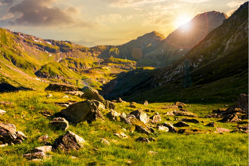 lovely scenery of Transfagarasan road in valley at sunset. rocks on grassy meadow and slopes. half of the valley in shade of mountain ridge