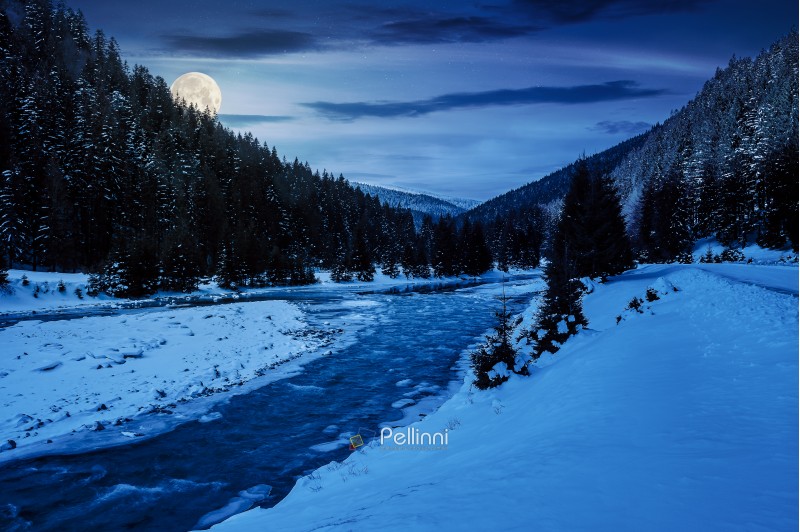 mountain river in winter at night in full moon light. snow covered river banks. forest in snow on the distant mountain. cloudy morning