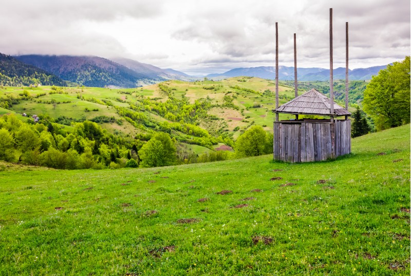 old wooden hay shed on grassy hillside. beautiful scenery of mountainous rural area in springtime
