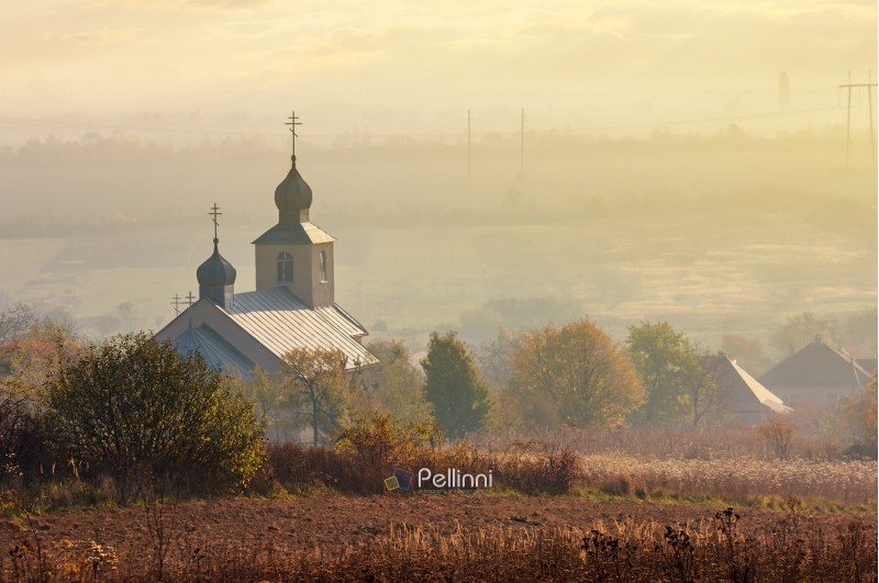 orthodox church on a hill above the foggy rural valley at sunrise. lovely countryside scenery in autumn