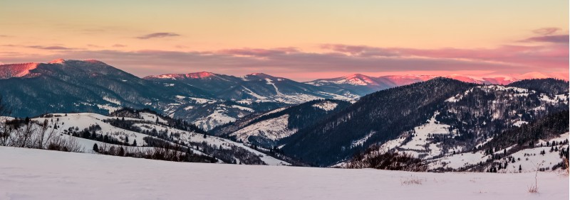 panorama of mountain ridge at dawn in winter. beautiful landscape with forested hills in snow. clouds on sky and mountain tops lit by red rising sun