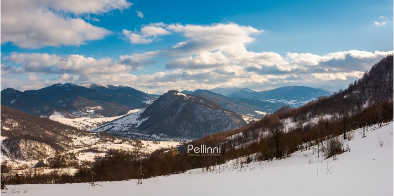 panorama of winter countryside in mountains. wonderful sunny day with gorgeous cloudscape. dark forest on the snow covered hills. village down in the distant valley. faraway ridge with snowy tops