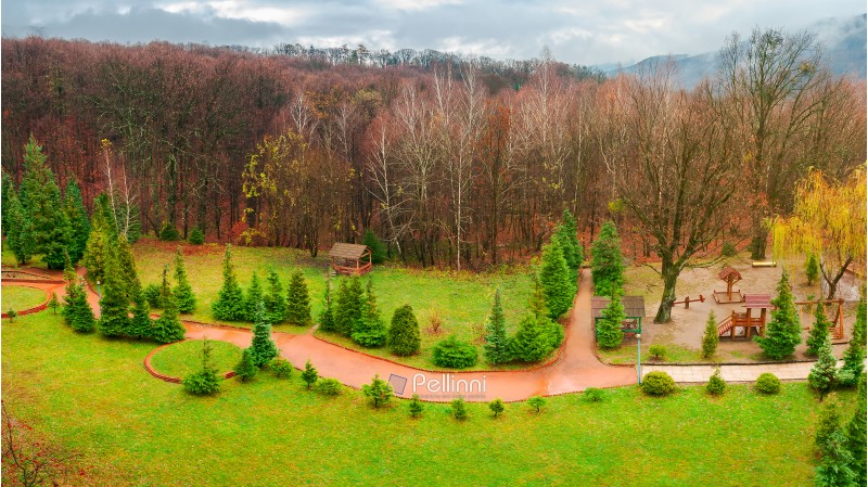 park with playground in autumn. gloomy rainy weather in mountains. green lawn and leafless forest in november