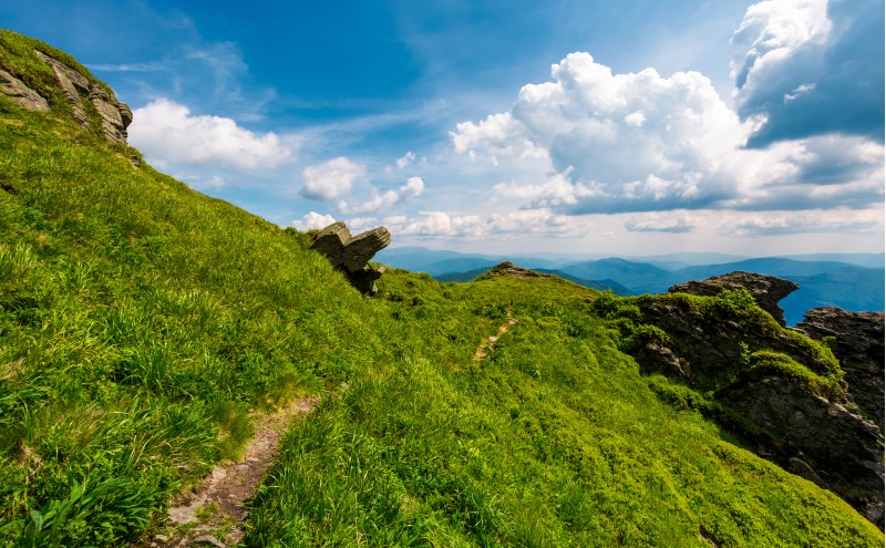 path to the edge of a hill. beautiful mountainous landscape with grassy hillside and giant boulders under. fine weather with blue sky and some clouds