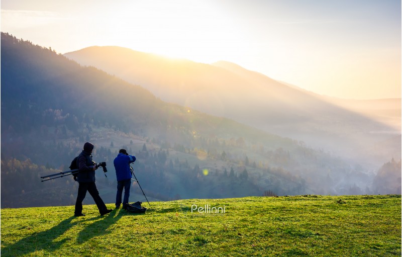 photographers on workshop at sunrise. capturing gorgeous scenery of mountainous area from the top of grassy hill. beautiful landscape with sun rising behind the forested mountain and foggy valley