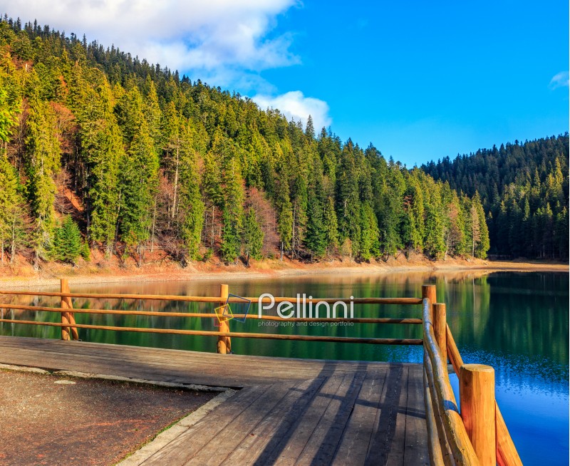 pier with fence on the Lake in mountain near coniferous forest in autumn sunset