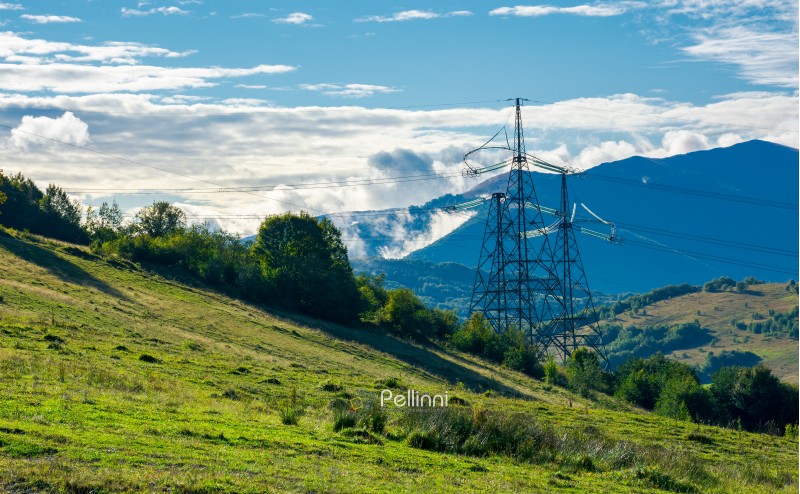 power line tower on the hill. huge mountain in clouds in the distance. autumn countryside