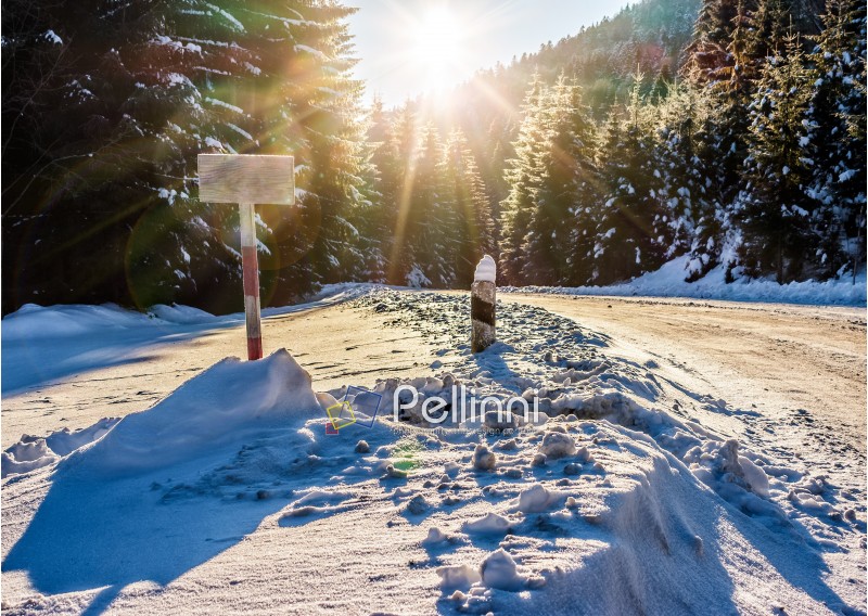 winter mountain landscape. wooden road sign on winding road that leads into the spruce forest covered with snow at sunrise