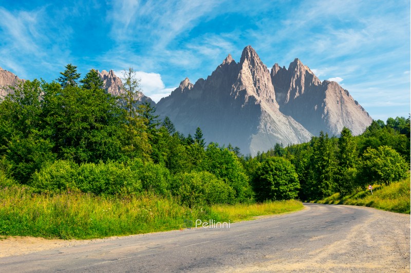 road through forest in to the mountains. composite mountainous landscape with rocky peaks in the distance. beautiful summer nature with gorgeous sky. travel and explore unknown places concept