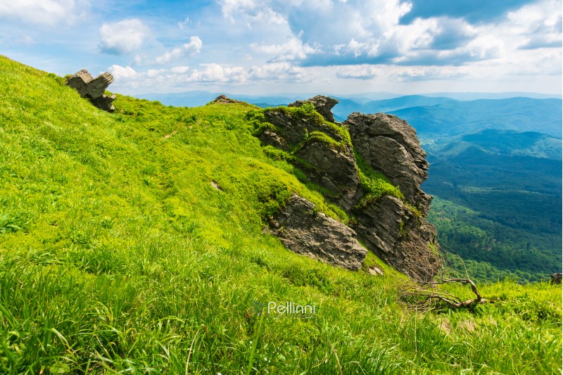 rocky formation on a grassy hillside. path among the grass to the boulders. beautiful mountain ridge in the distance. wonderful summer weather. fluffy clouds on the blue sky