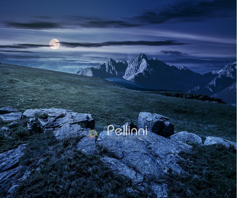 Composite night landscape with full moon. rocky peaks of mountain ridge and rocks on hillside under the dark sky with clouds and stars. picturesque fantasy view.