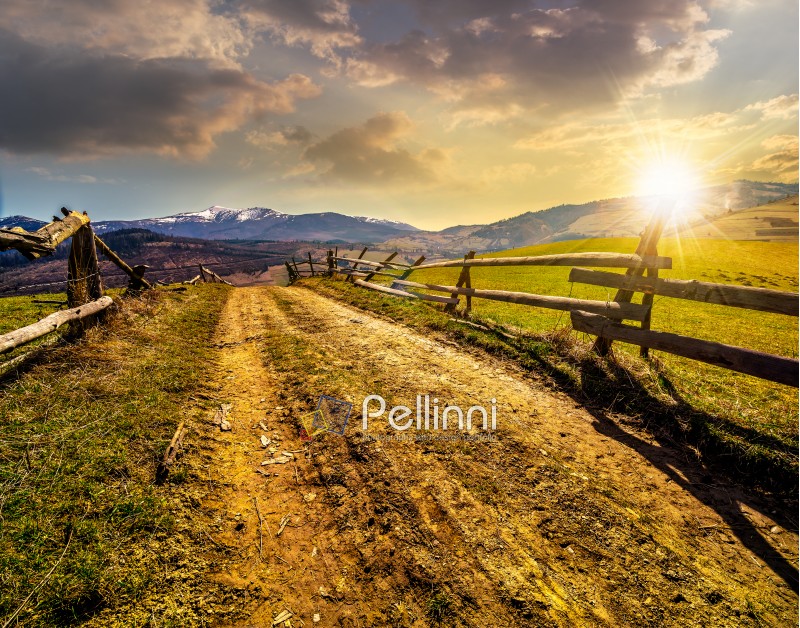 fence near the road through the  rural meadow in mountain region in spring time in evening light