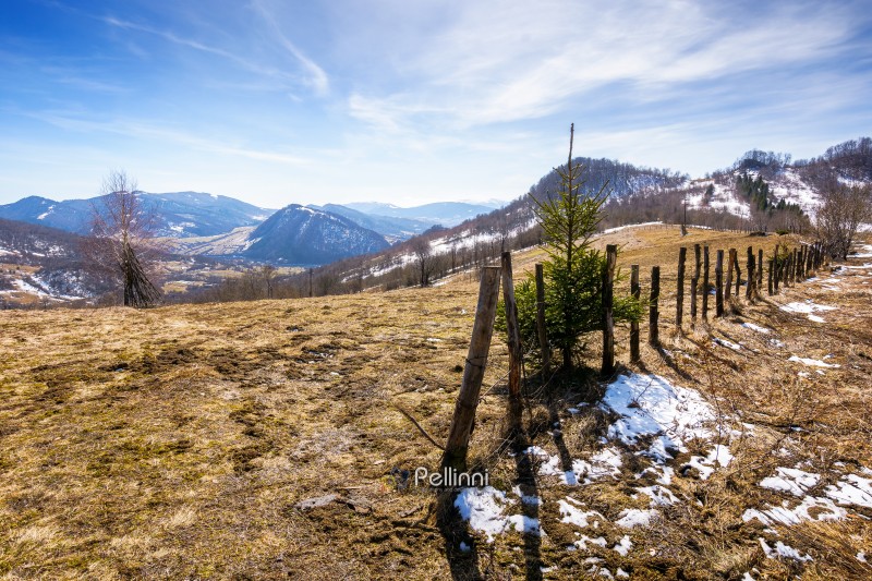 rural landscape of carpathian mountains in early spring under blue sky. snow covered hill with barbed wire fence on a sunny day. green environment sustainability and protection. background for earth day