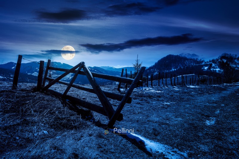 rural landscape of carpathian mountains in early spring under dark sky at night. snow covered hill with barbed wire fence in full moon light. inner strength to overcome fear, loneliness in darkness