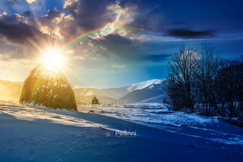 rural scenery with haystack in winter. day and night time change concept. countryside landscape with snow covered hill in mountains with sun and moon at twilight. low angle view with snowy peak in the background. duality and transition template. freshness concept