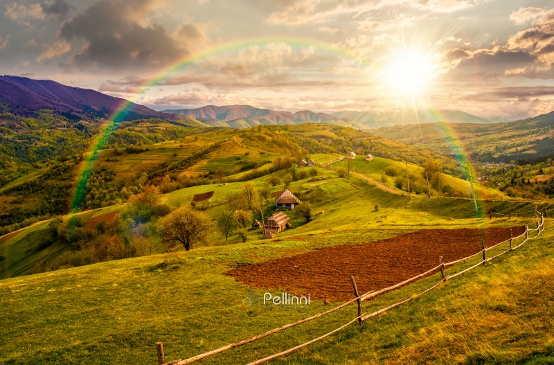 scenic view of arable and wooden fence on hillside in rural area at sunset. beautiful countryside mountain landscape in spring in evening light. storytelling cinematic image under the rainbow