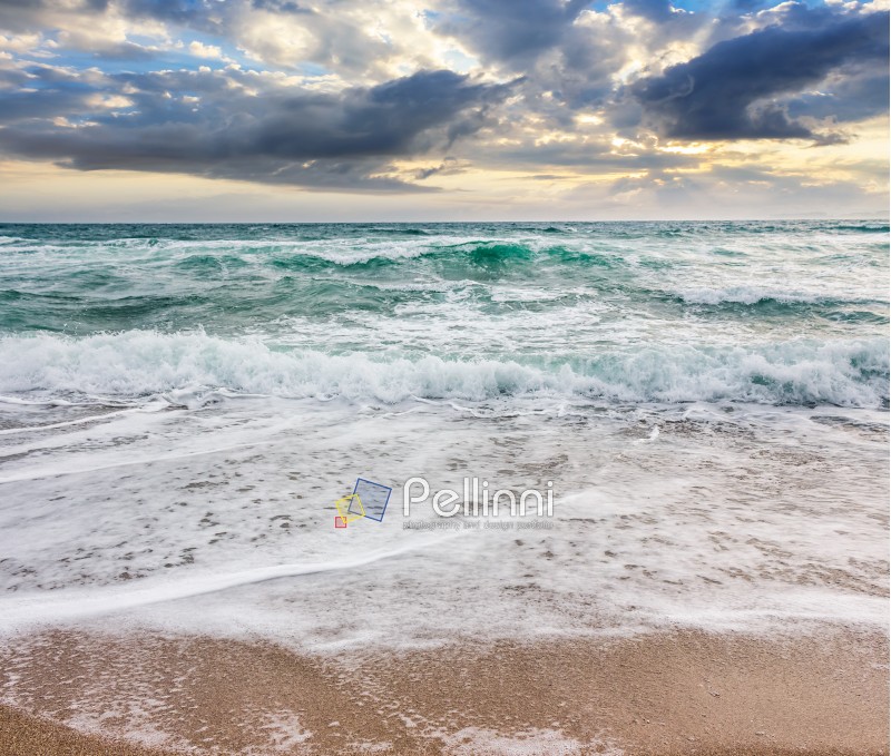 seascape in stormy weather at cloudy sunrise. green waves crashing on golden sand of the beach