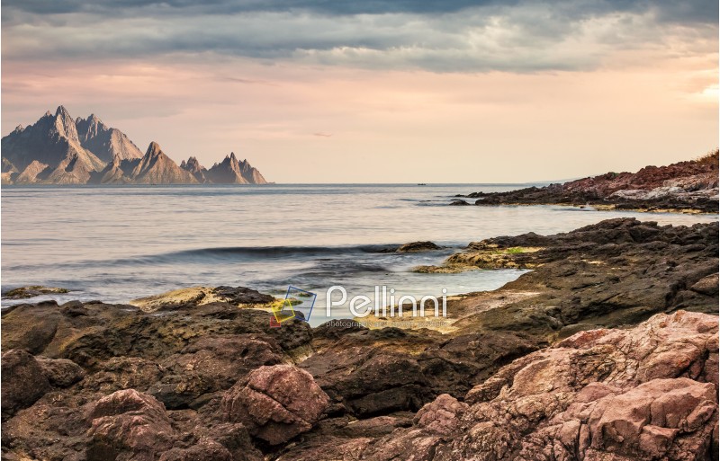 seascape with rocky coast and mountain ridge with high peaks. composite landscape with cloudy sky at menacing sunrise