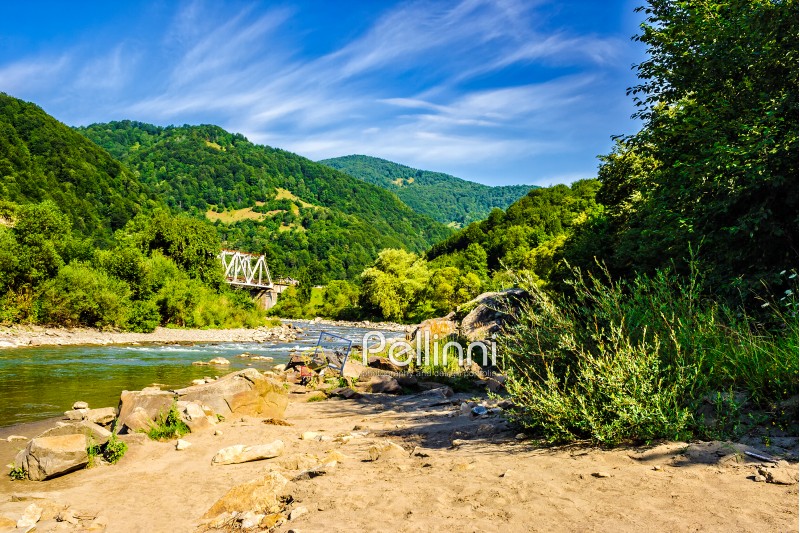 shore of a mountain river with stones and iron bridge among the forest in fural area