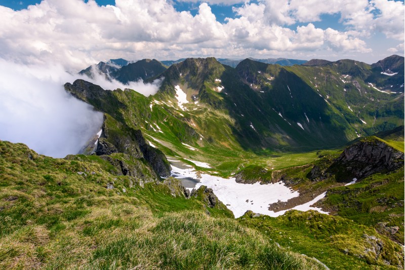 snow in the valley of Fagaras mountains. beautiful summer scenery on a cloudy day. dappled light on grassy slopes