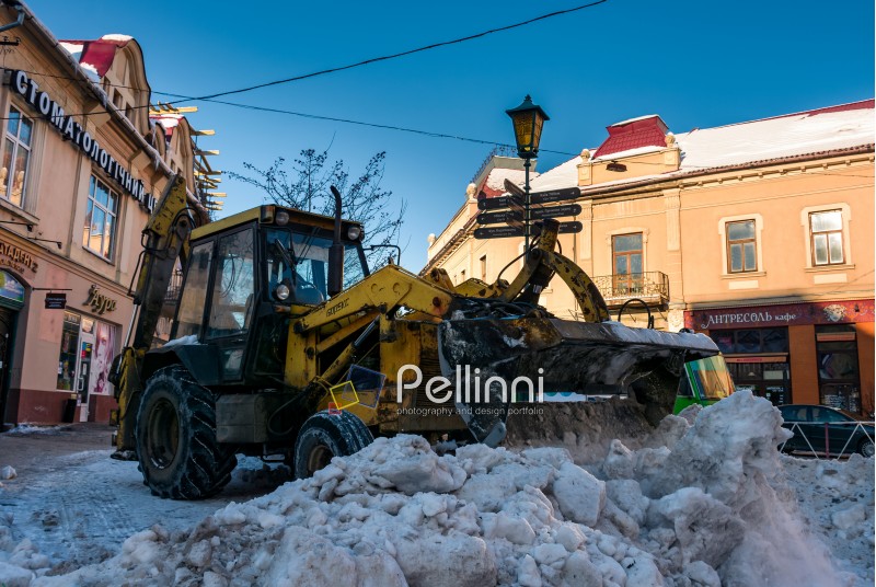 Uzhgorod, Ukraine - January 19, 2017: snow removal on streets of old town. people remove snow huge amount of snow with the help of  tractor with snowplow