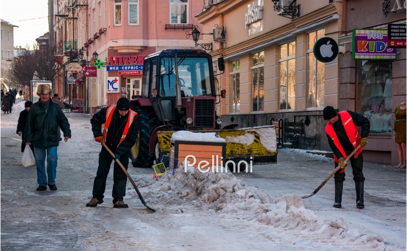 Uzhgorod, Ukraine - January 19, 2017: snow removal on streets of old town. people remove snow huge amount of snow with the help of shovels and tractor