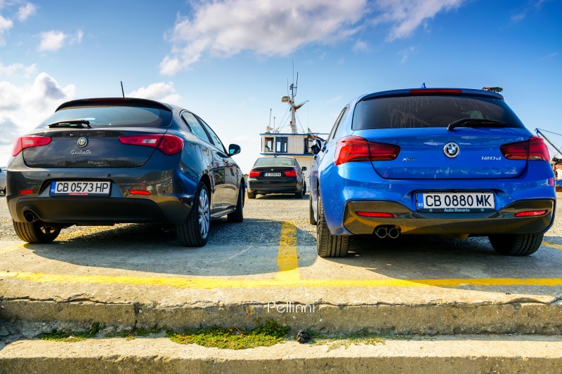 sozopol, burgas, bulgaria - 05 sep 2019: two hatchback cars parked in port. black alfa romeo giulietta and blue bmw 120d xdrive view from the back. italy vs germany and street racing concept