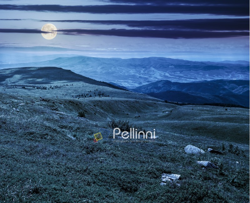 mountain landscape with stones laying among the grass on the hill side at night in full moon light