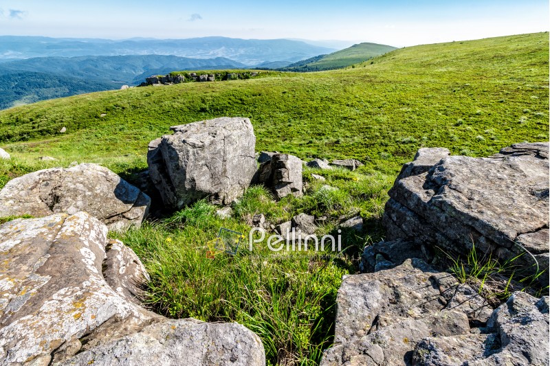 mountain landscape with stones laying among the grass on top of the hill side under the cloudy summer sky