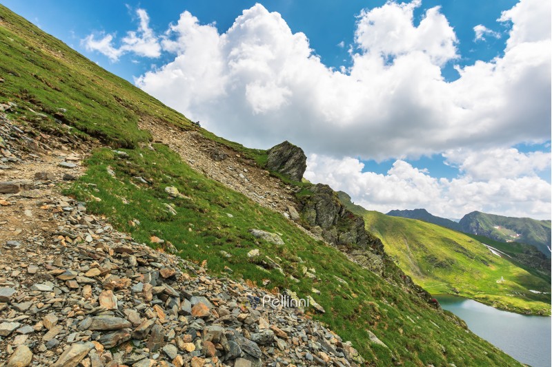 summer time in romanian carpathians. beautiful landscape of fagaras mountains. lake capra down in the valley. fluffy clouds above the ridge. rocky cliff on the hillside