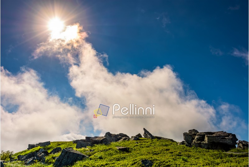 sunburst on a blue sky with clouds over the mountains with rocky hillside